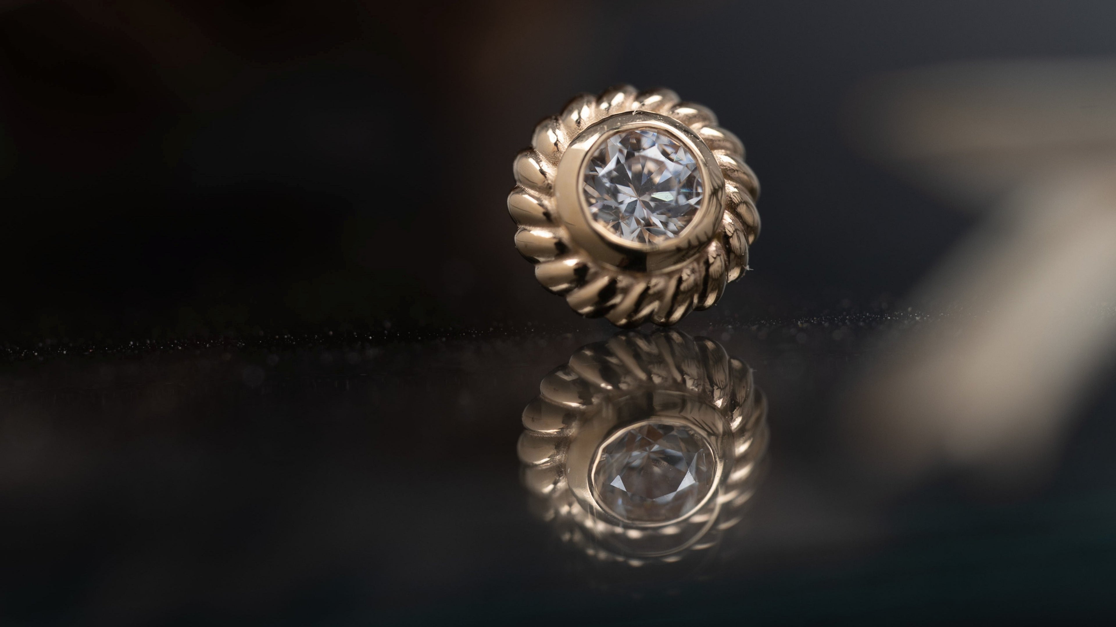 Gold earring with a diamond on a reflective surface