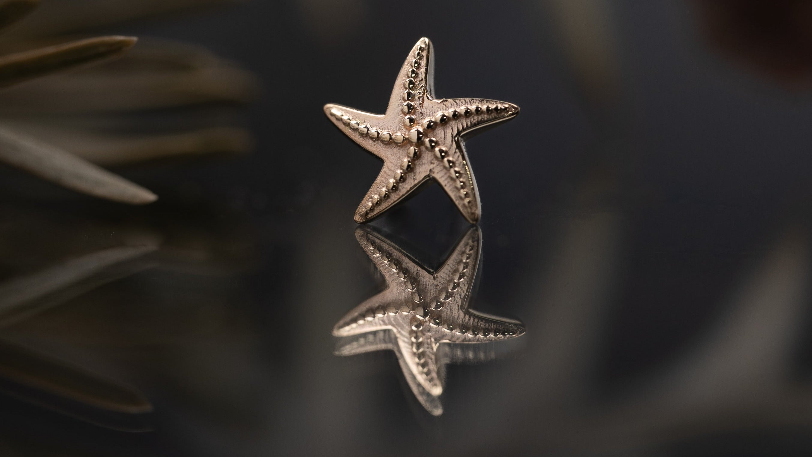 Silver starfish-shaped earring on a reflective surface with blurred natural background