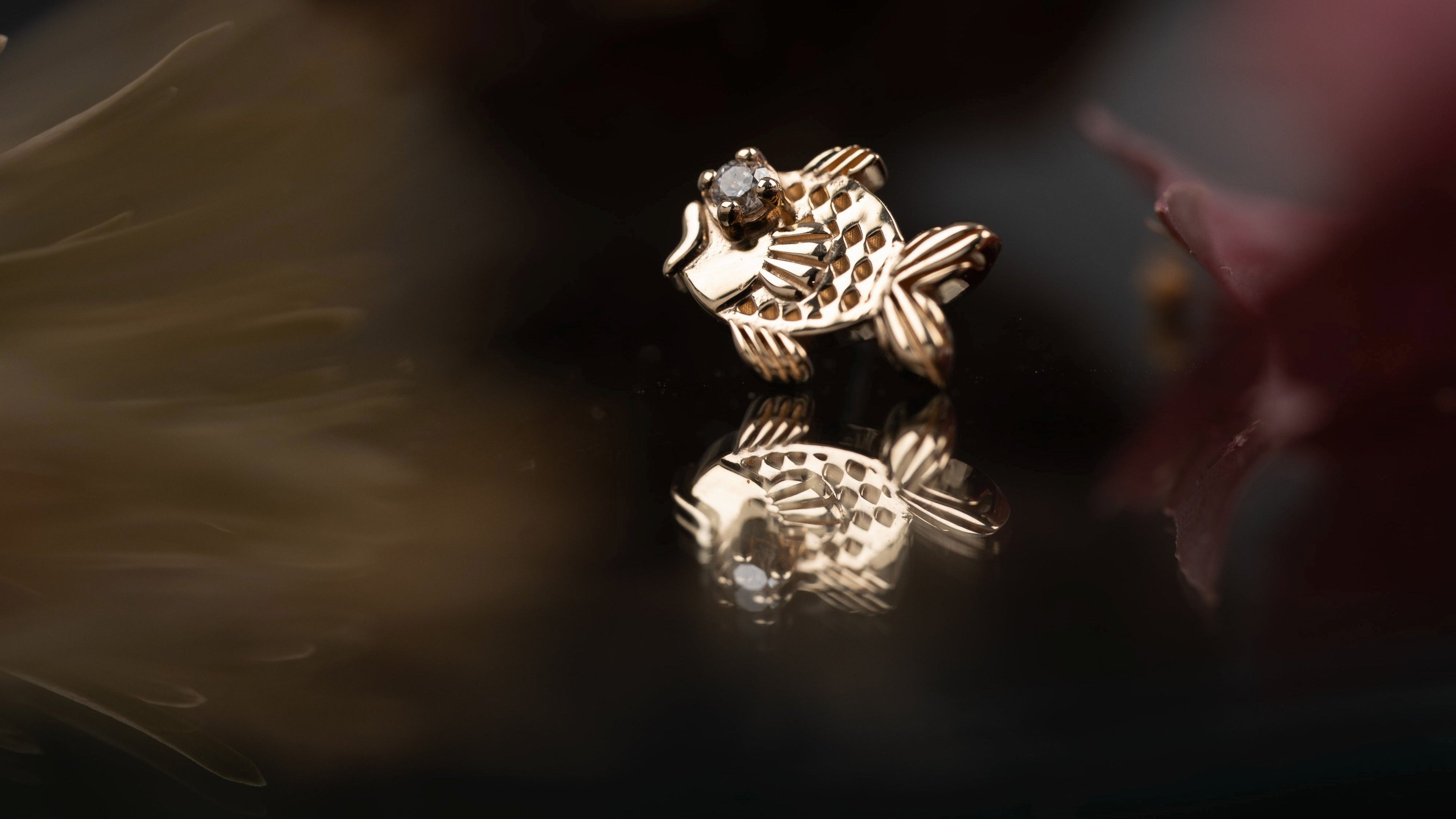 Gold earring with a diamond on a reflective surface with a dark background