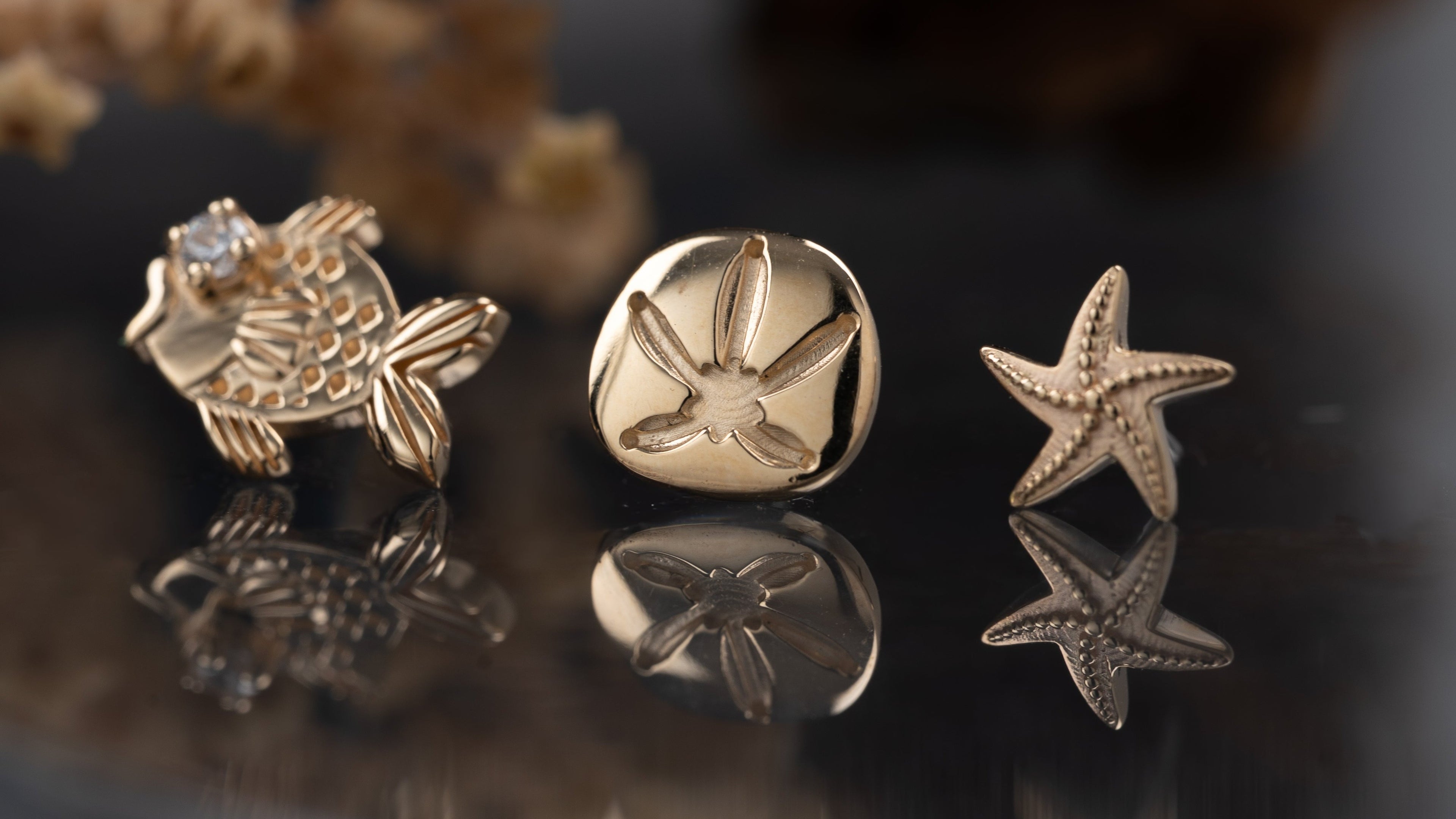 Three gold jewelry pieces on a reflective surface with a blurred natural background