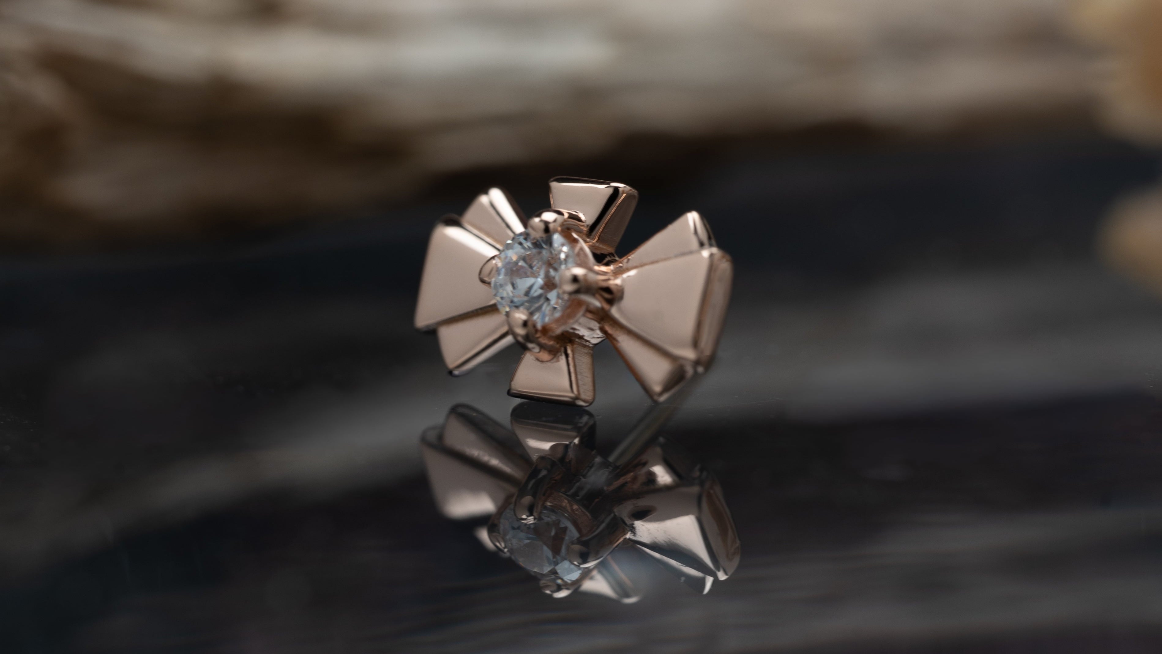 Rose gold earring with a diamond on a reflective surface