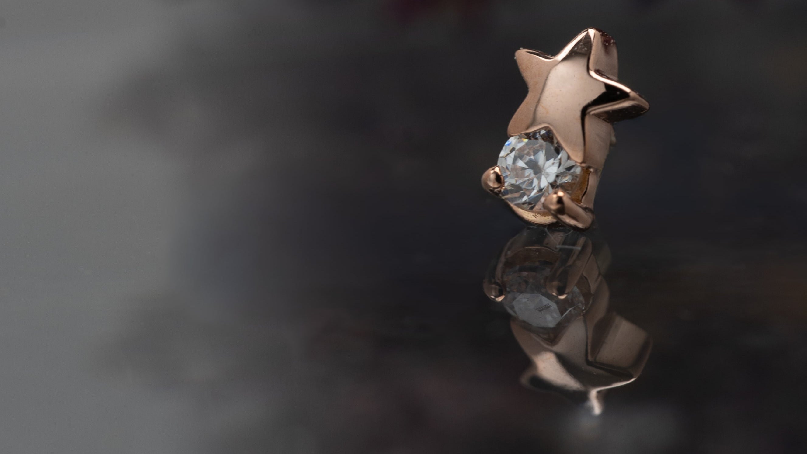 Star-shaped rose gold earring with a clear gemstone on a reflective surface.