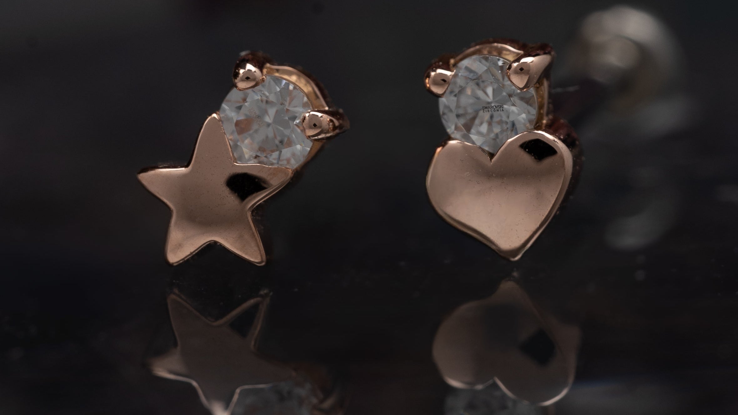 Rose gold star and heart-shaped earrings with clear gemstones on a reflective surface.