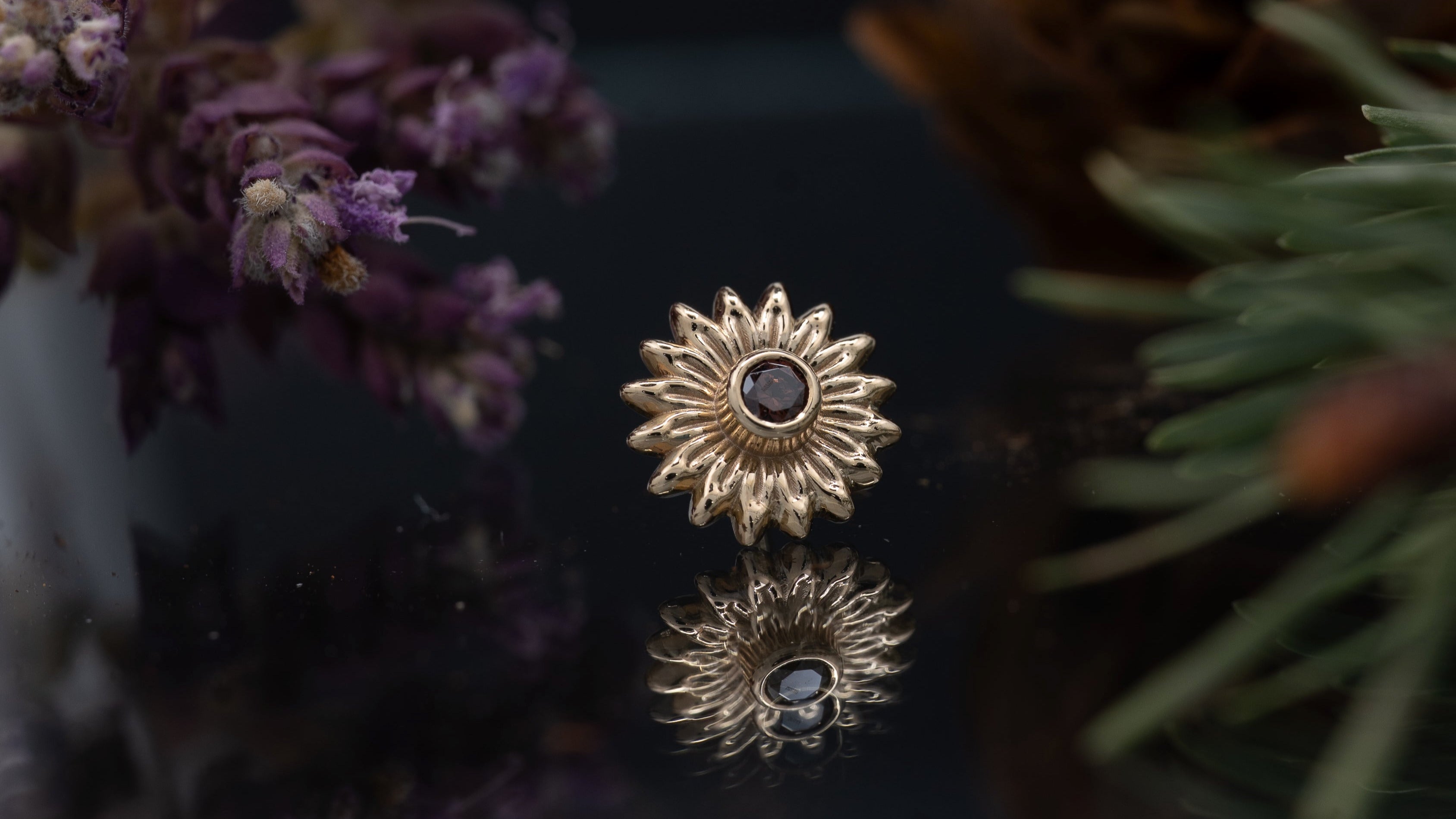 Gold sunflower-shaped earrings with a central gemstone on a dark surface with decorative elements.