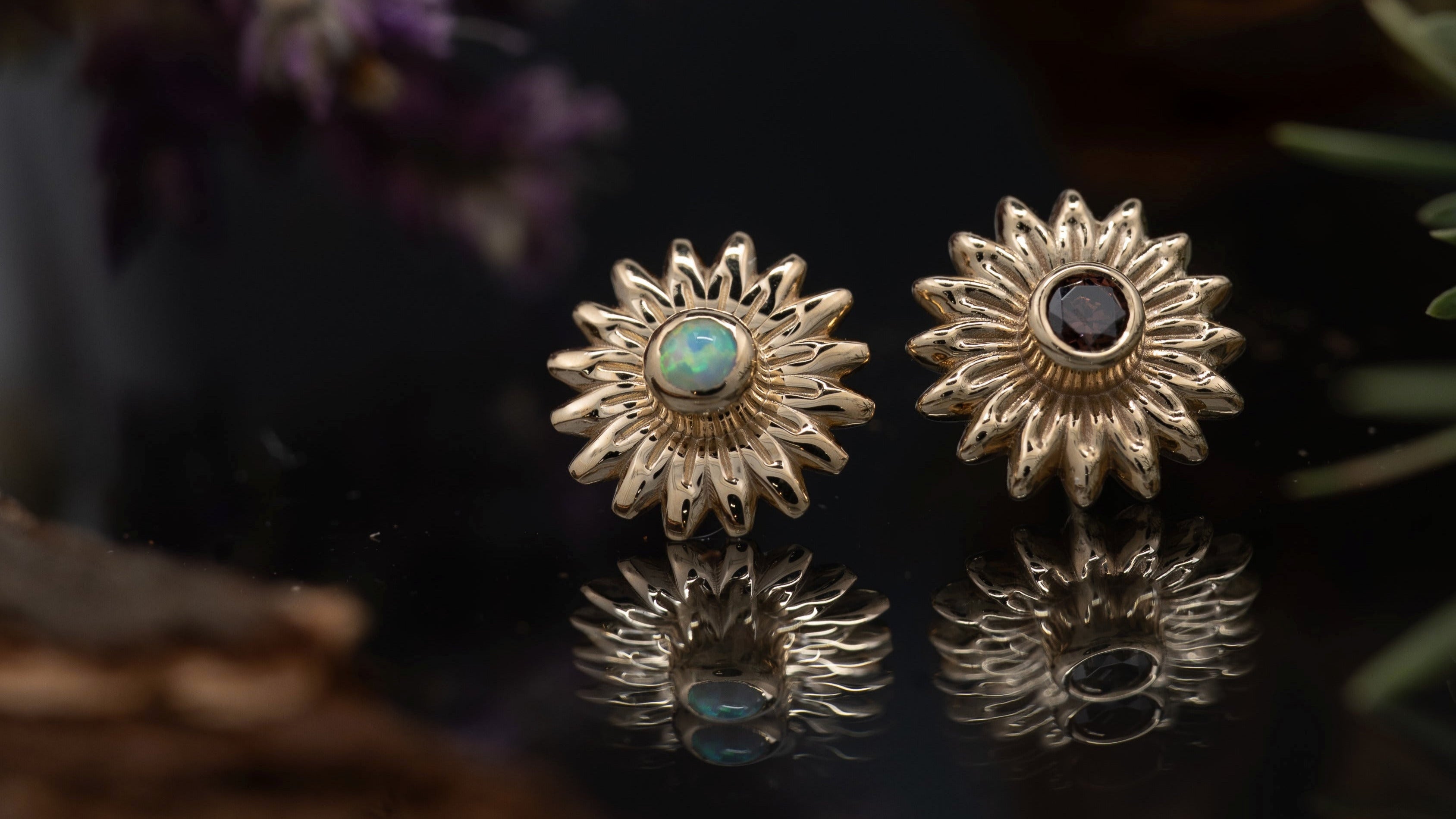 Gold sun-shaped earrings with gemstones on a reflective surface with a dark background