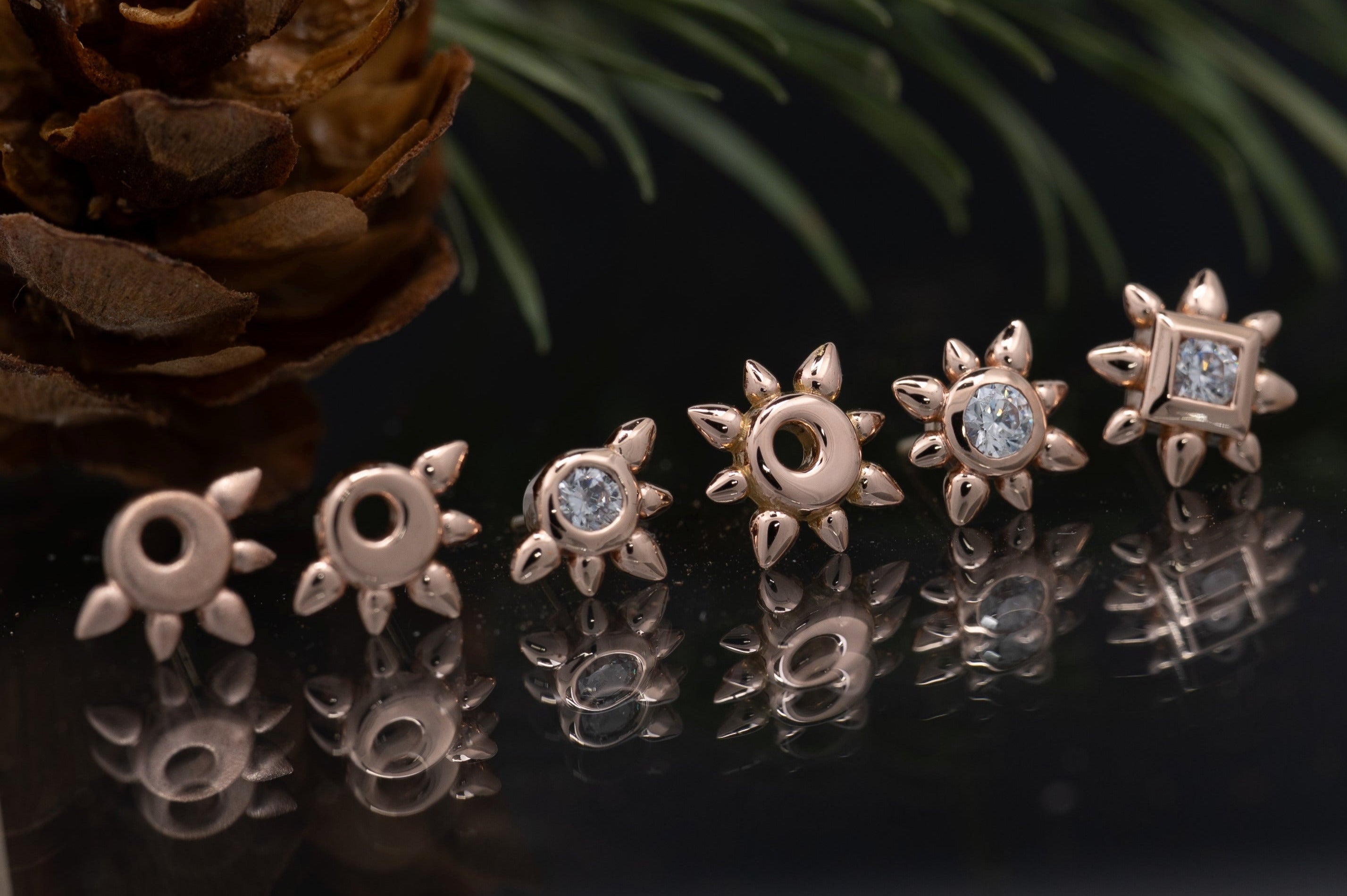 Pair of star-shaped earrings on a reflective surface with a pine cone and branch in the background.
