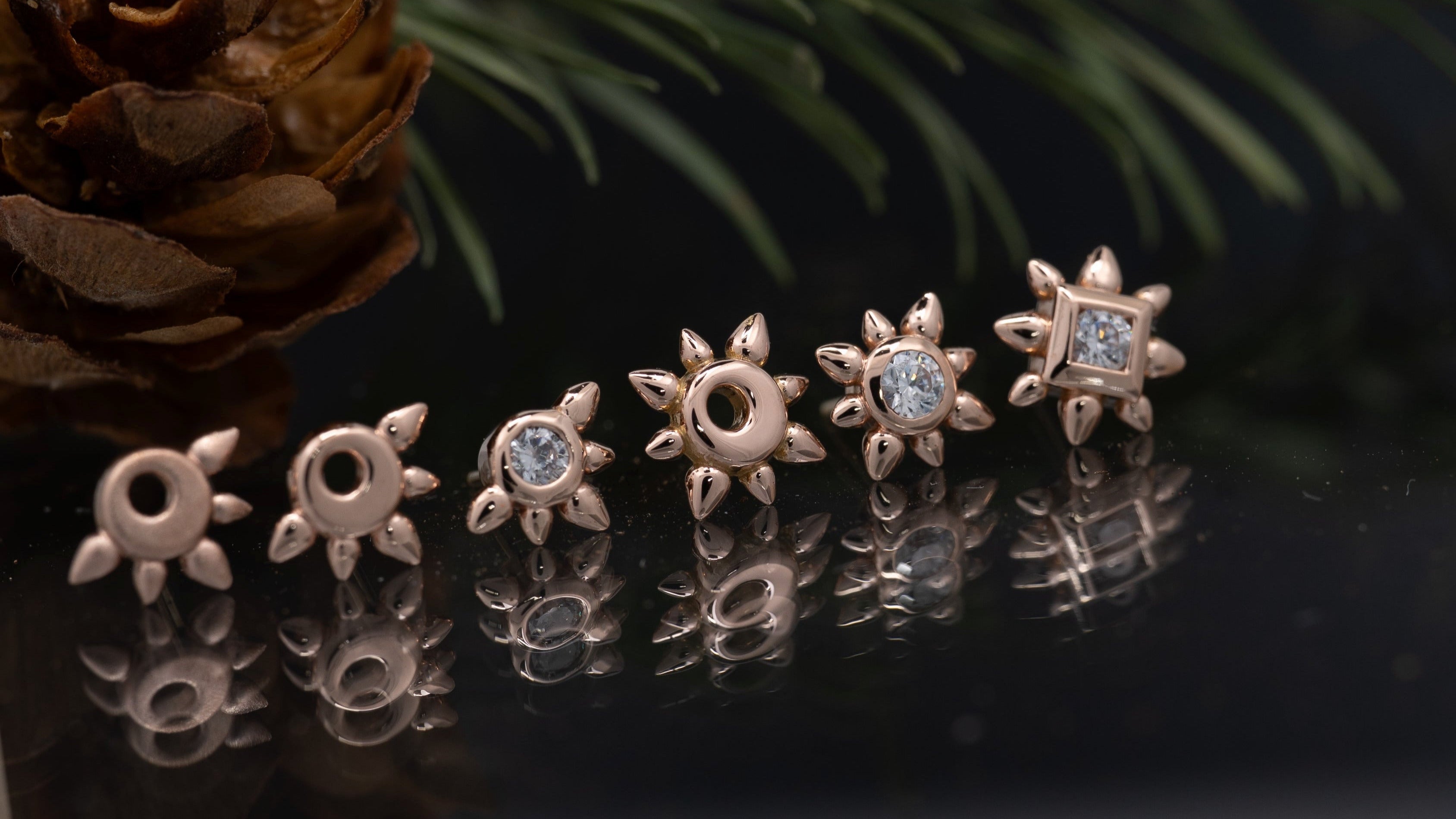 Pair of star-shaped earrings on a reflective surface with a pine cone and branch in the background.